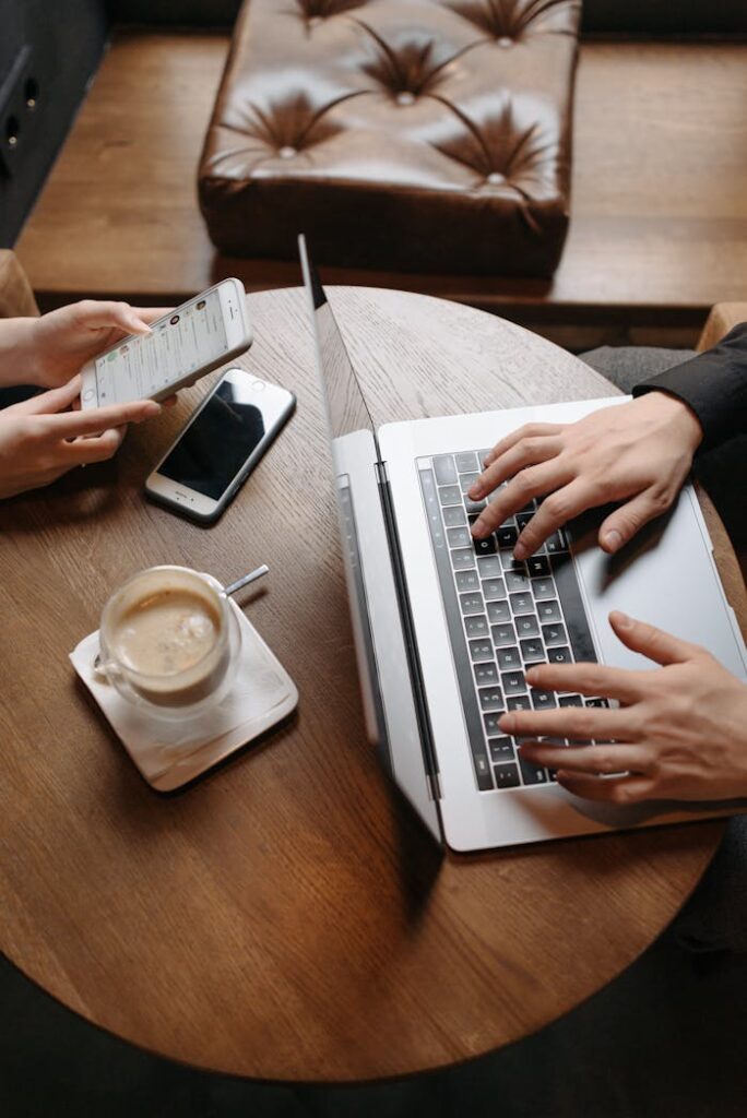 Two people working together in a cafe, using a laptop and smartphone on a wooden table.